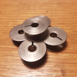 Könnte beinhalten: Fünf silberne Metallspulen für eine Nähmaschine.