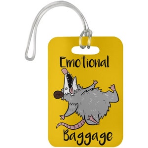 Könnte beinhalten: Gelber Gepäckanhänger mit einem Karikatur-Opossum und dem Text "Emotional Baggage".