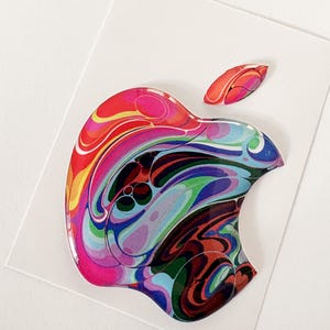 Puede incluir: Una pegatina colorida con el logotipo de Apple. La manzana presenta un vibrante diseño en espiral de tonos rojos, rosas, amarillos, azules, verdes y morados, sobre un fondo blanco.