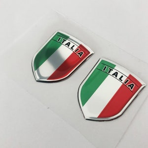 May include: Two silver shield-shaped stickers with the Italian flag colours of green, white, and red. The word "ITALIA" is printed in black on each sticker.