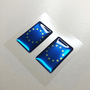 Könnte beinhalten: Zwei rechteckige Aufkleber mit der Flagge der Europäischen Union in Blau und Gelb. Die Aufkleber haben eine glänzende Oberfläche.