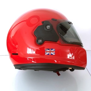 May include: A glossy red motorcycle helmet with a dark visor and black accents. The helmet features a small Union Jack sticker on the side. The helmet is designed for safety and protection.