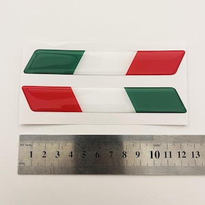 May include: Two 3D Italian flag stickers, each with a green, white and red stripe. The stickers are approximately 13 cm long.