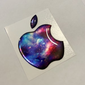 Può includere: Un adesivo con logo Apple a tema galassia con un design a nebulosa blu, viola e rosso. L'adesivo è su uno sfondo bianco.