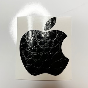 May include: Black and white sticker of an apple with a crocodile skin pattern.