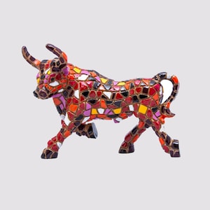 May include: A colourful mosaic bull figurine in a walking pose. The mosaic is made up of red, orange, yellow, purple, and black pieces. The bull's horns and hooves are dark brown. The mosaic pieces are outlined with a gold-coloured material.