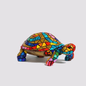 Op de afbeelding: Decoratief schildpadbeeldje met een mozaïekontwerp. De schild is voorzien van een levendig patroon van goud, blauw, rood, geel en roze. De poten en kop zijn ook fel gekleurd. Het beeldje staat tegen een witte achtergrond.