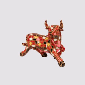 Pode incluir: Estatueta decorativa de touro com design de mosaico. O touro é principalmente vermelho, rosa, amarelo e castanho, com um padrão de mosaico. A estatueta tem chifres e está em pose de corrida. O logotipo da Casa de Souvenirs está no canto superior esquerdo.