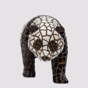 May include: A ceramic panda figurine with a mosaic-like pattern in black, white, and brown. The panda has black ears and eyes, and the mosaic design covers its body. The figurine is a decorative item.
