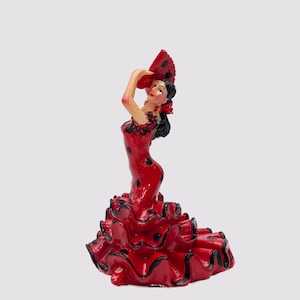 May include: A ceramic figurine of a flamenco dancer in a vibrant red dress with black polka dots and ruffled skirt. The dancer holds a fan, with black hair and a red flower. The figurine is a souvenir.