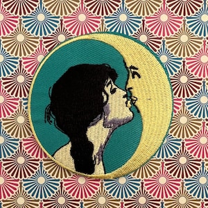 Könnte beinhalten: Ein gestickter Aufnäher mit einer Frau mit dunklen Haaren, die einen zunehmenden Mond küsst. Der Mond ist gelb und das Gesicht der Frau ist weiß. Der Hintergrund ist türkis.