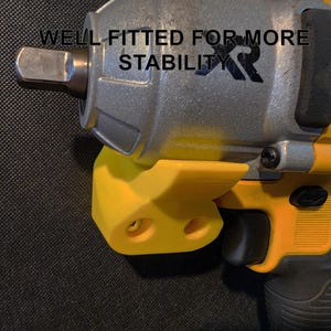 May include: A yellow and black impact wrench with a yellow plastic holder. The holder has two holes for mounting. The wrench has the text "WELL FITTED FOR MORE STABILITY XR" printed on it.