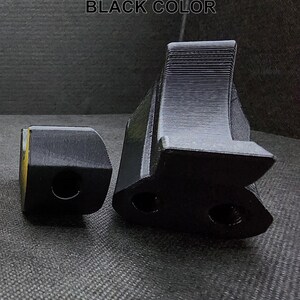 May include: Two black plastic 3D printed objects. The larger object has a curved shape with two holes. The smaller object is a rectangular block with a hole in the center.