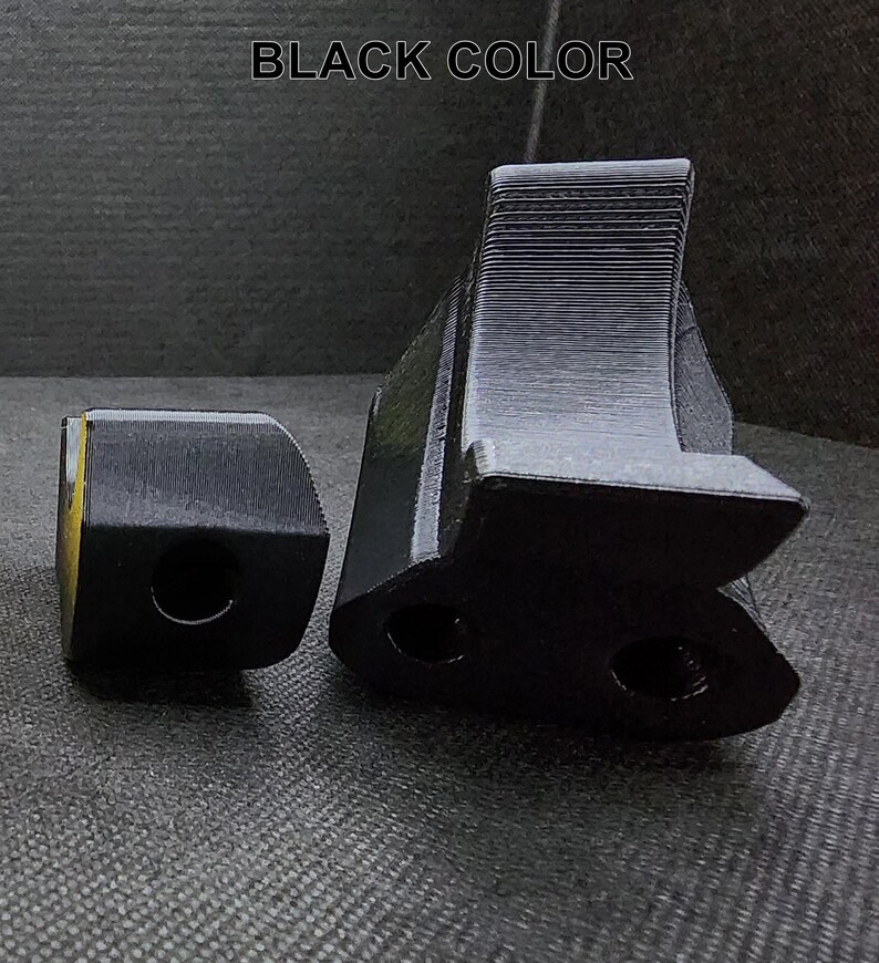 May include: Two black plastic 3D printed objects. The larger object has a curved shape with two holes. The smaller object is a rectangular block with a hole in the center.