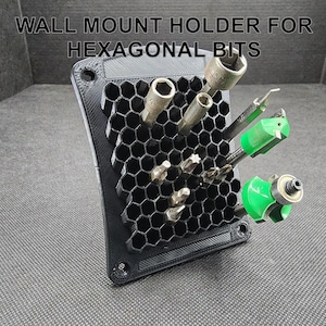 May include: A black wall mount holder for hexagonal bits. The holder has a honeycomb design and is filled with various bits, including a green and black router bit.