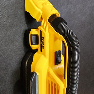 Puede incluir: Una aspiradora DeWalt 20V Max amarilla con una manguera negra y un interruptor de encendido negro. La aspiradora está montada en una pared.