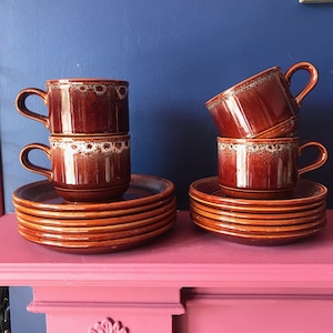 May include: Two stacks of brown and white ceramic coffee cups with a brown and white floral pattern. The cups are stacked on top of brown and white saucers. The saucers are stacked on top of each other to create a tower of cups and saucers.