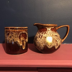 May include: A brown and white ceramic creamer and sugar set with a mottled glaze. The creamer has a handle and a spout. The sugar bowl has a lid.