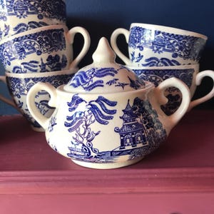 May include: A blue and white porcelain sugar bowl with a lid. The bowl features a traditional Chinese design with a pagoda and willow tree.