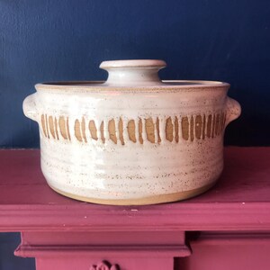 May include: A white ceramic casserole dish with a lid. The dish has a brown stripe design around the top edge.