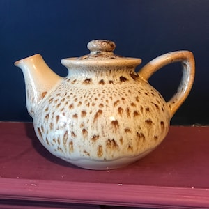 May include: A brown and white speckled ceramic teapot with a lid. The teapot has a rounded body and a handle.
