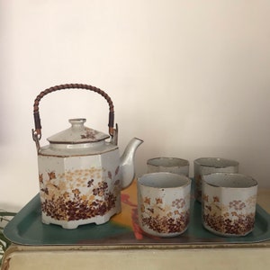 May include: A white ceramic teapot with a brown wicker handle and floral pattern, along with four matching teacups.