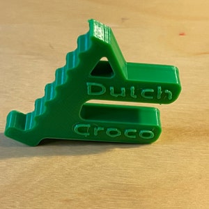 Könnte beinhalten: Ein grüner Plastik-Türstopper in Form eines Krokodils mit der Aufschrift "Dutch Croco".