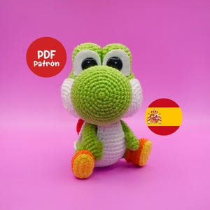 Può includere: Una bambola Yoshi all'uncinetto fatta a mano in verde, bianco, arancione e rosso. La bambola ha grandi occhi neri ed è seduta. Un cerchio rosso con il testo "PDF Patrón" è in alto a sinistra. Una bandiera spagnola è in basso a destra.