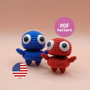Puede incluir: Dos figuras de ganchillo, una azul y otra roja, con grandes ojos blancos y negros. Las figuras tienen brazos y piernas pequeños, sobre un fondo melocotón. Un círculo rosa con el texto "PDF Pattern" es visible. También es visible una pegatina de la bandera estadounidense.