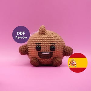 May include: A crocheted brown character with a smiling face, black eyes, and small arms and legs. The character is on a pink background. A purple circle with the text "PDF Patrón" is in the upper left corner. A Spanish flag is in the lower right corner.