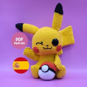 以下が含まれることがあります： 黒い先端の耳、赤い頬、黒い目を持つ黄色の編みぐるみピカチュウ人形。赤、白、黒のモンスターボールを持っています。画像には「PDF Patrón」というテキストとスペインの国旗が含まれています。