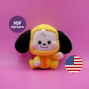Könnte beinhalten: Ein gehäkeltes Plüschtier mit weißem Gesicht, schwarzen Augen, einer kleinen schwarzen Nase und rosa Wangen. Es trägt ein gelbes Kapuzenoutfit mit schwarzen Ohren, zwei orangefarbenen Knöpfen auf der Brust und weißen Händen. Ein violetter Kreis zeigt PDF Pattern.