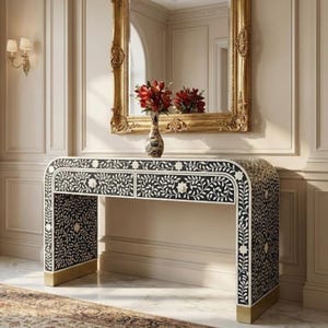 May include: A black and white floral patterned console table with two drawers, gold accents, and a gold framed mirror above it. A vase of red flowers sits on the table. The room has a classic, elegant style.