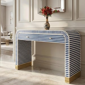 May include: A modern console table with a navy and white striped design. The table has two drawers with gold-colored hardware and gold accents on the legs. A vase with red flowers sits on top of the table.