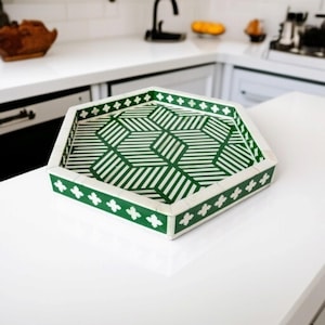 May include: A hexagonal tray with a green and white geometric pattern. The tray has a white border with a repeating floral design.