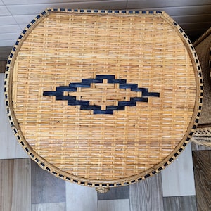 May include: A round, woven wicker table in natural tan. It has a navy blue diamond pattern in the centre and a navy blue border. The table is a decorative item. The diameter is approximately 60 cm.