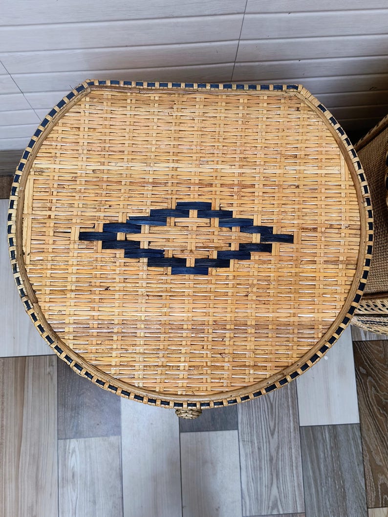 May include: A round, woven wicker table in natural tan. It has a navy blue diamond pattern in the centre and a navy blue border. The table is a decorative item. The diameter is approximately 60 cm.