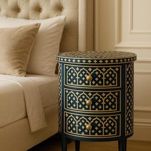Könnte beinhalten: Ein marineblauer Nachttisch mit drei Schubladen und einer runden Oberseite. Der Tisch hat goldene geometrische Muster und goldene Knöpfe. Der Tisch ist etwa 61 cm hoch.