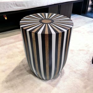 Può includere: Un tavolino rotondo in legno con strisce bianche e nere e un design a raggiera sulla parte superiore.