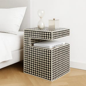 May include: A modern nightstand with a black and white checkered pattern. The nightstand has two levels, with a book and decorative items on top. The book has the text "TABLECONFANDY".