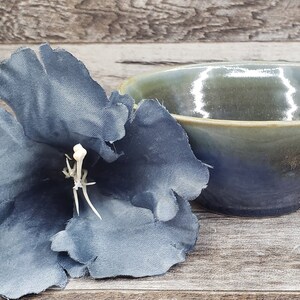 May include: A blue and green ceramic bowl with a glossy finish. The bowl is sitting on a wooden surface next to a blue fabric flower.