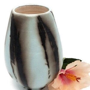 May include: A light blue ceramic vase with black streaks, featuring a delicate, light pink hibiscus flower.