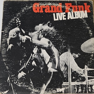 May include: A black and white photograph of a rock band, Grand Funk, on the cover of their album "Live Album".