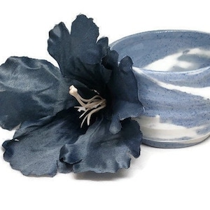 May include: A small, blue and white ceramic bowl with a swirling pattern. The bowl is sitting next to a dark blue flower.