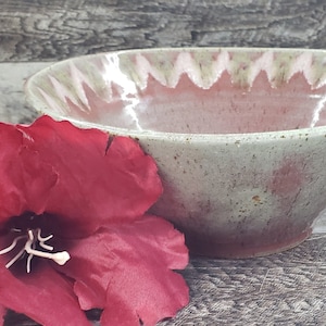 Puede incluir: Un tazón grande de cerámica con un esmalte verde y rosa. El tazón tiene un borde ondulado y festoneado y un acabado moteado.