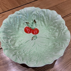 Könnte beinhalten: Eine grüne Salatschüssel aus Keramik mit einem Salatblatt-Design und zwei roten Tomaten. Die Schüssel ist perfekt zum Servieren von Salaten oder anderen Gerichten.