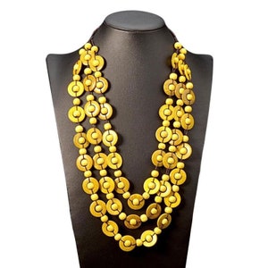 Könnte beinhalten: Eine mehrreihige Halskette aus gelben Holzperlen in Kreisform. Die Halskette wird auf einer schwarzen Mannequin-Büste präsentiert.