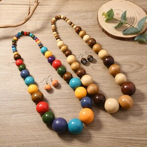May include: Two beaded necklaces and two pairs of earrings. One necklace is multi-colored, the other is a gradient of wood tones. The earrings are small, round, and have a dark brown pattern. The necklaces have large, round beads.
