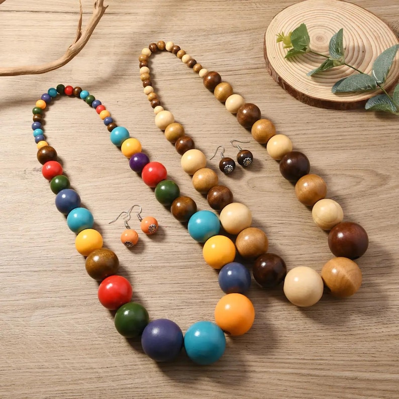 May include: Two beaded necklaces and two pairs of earrings. One necklace is multi-colored, the other is a gradient of wood tones. The earrings are small, round, and have a dark brown pattern. The necklaces have large, round beads.
