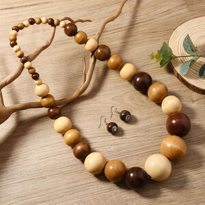 May include: A wooden bead necklace and matching earrings set. The necklace features large, round beads in shades of light tan, medium brown, and dark brown. The earrings have a small, round bead with a silver-colored accent.